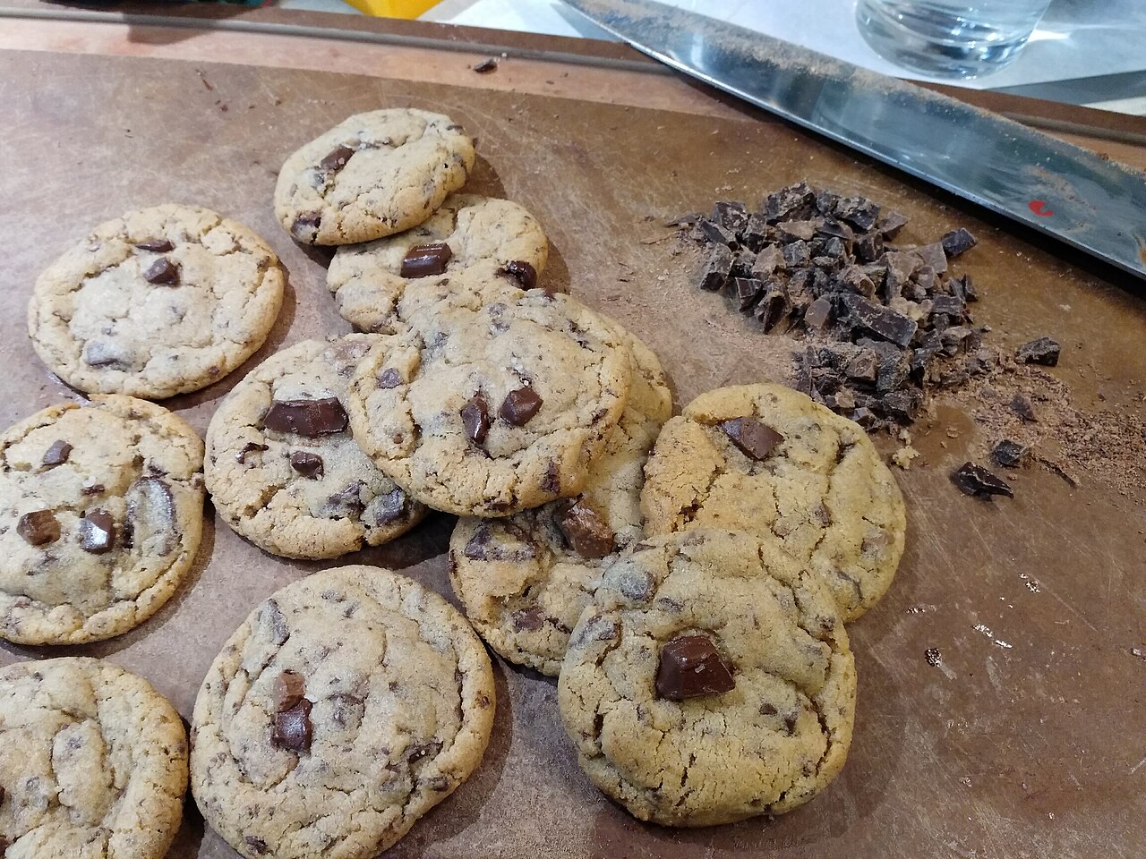 Chunky chocolate chip cookies beside chopped chocolate on a board